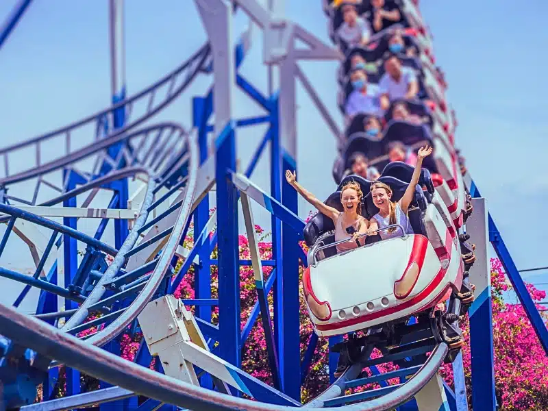 Two screaming girls on front of a roller coaster.